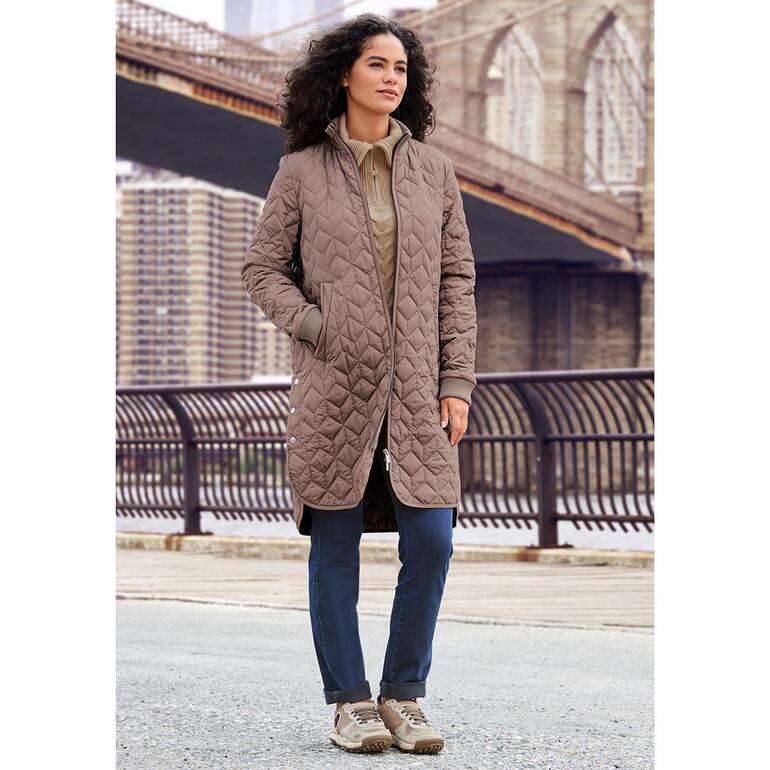 Sneakers durables Satorisan Femme en sneakers durables et manteau matelassé brun devant un pont en ville.