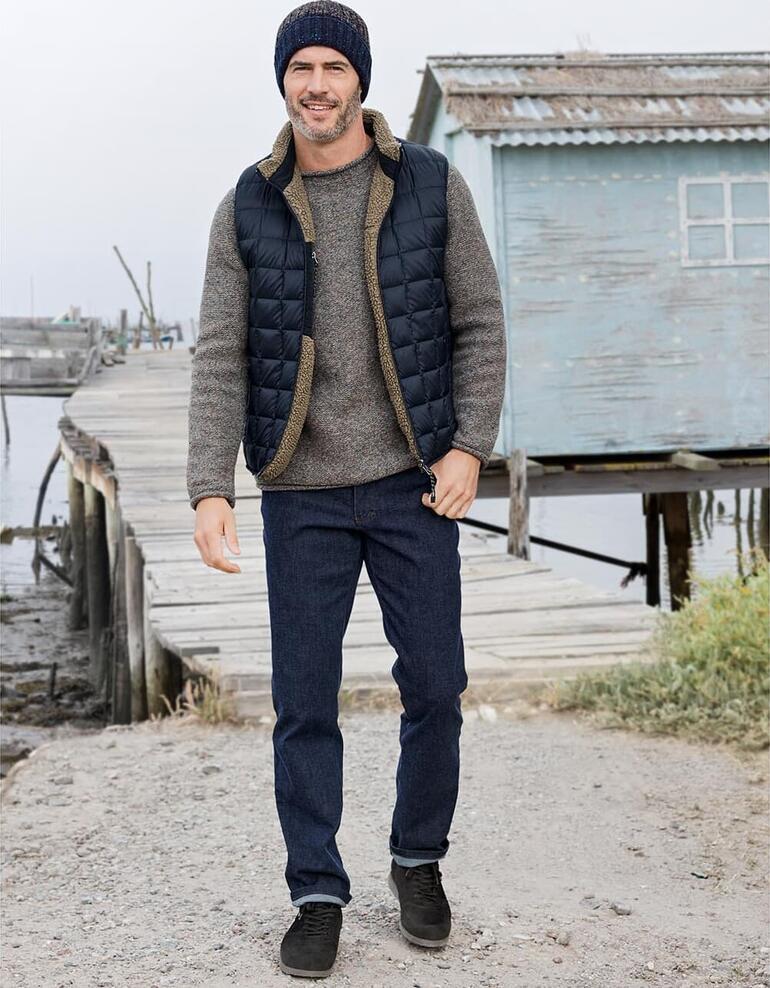 Pullover Donegal Fisherman Homme en gilet rembourré réversible, pull gris et bonnet se tenant au port.