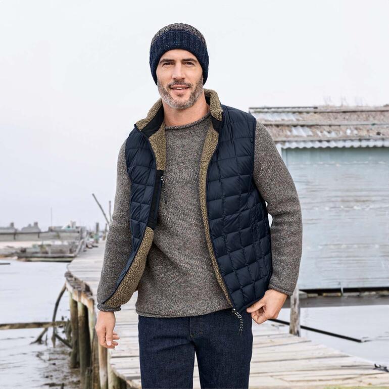 Homme en gilet rembourré réversible posant au port avec pull gris et bonnet.
