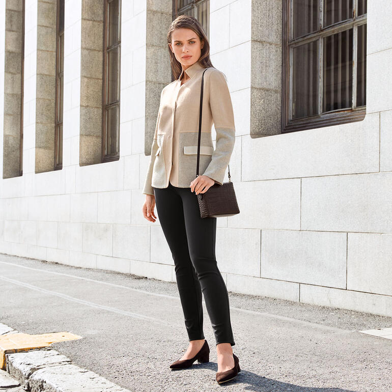 Femme en blazer en alpaga avec poche, adossée à un mur.