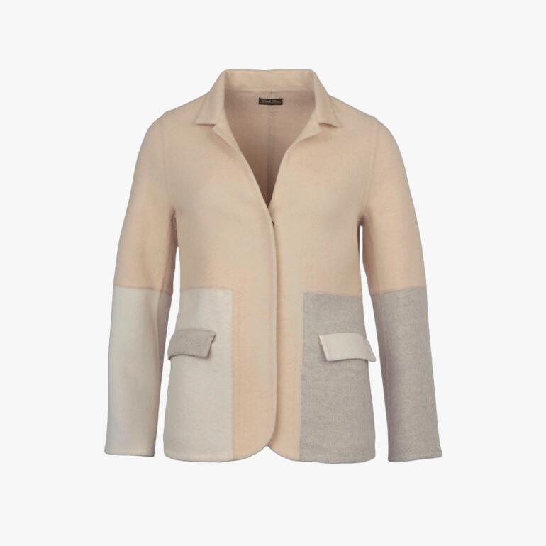 Femme portant un blazer colorblock beige et gris, debout devant un mur.