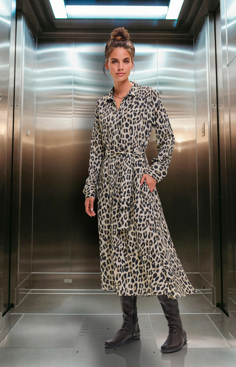 Femme en robe léopard se tient dans un ascenseur.