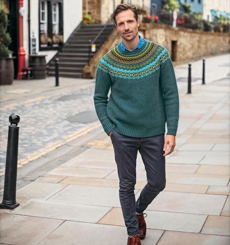 Homme portant un pull Fair-Isle d'Eribé, souriant devant un paysage rural.