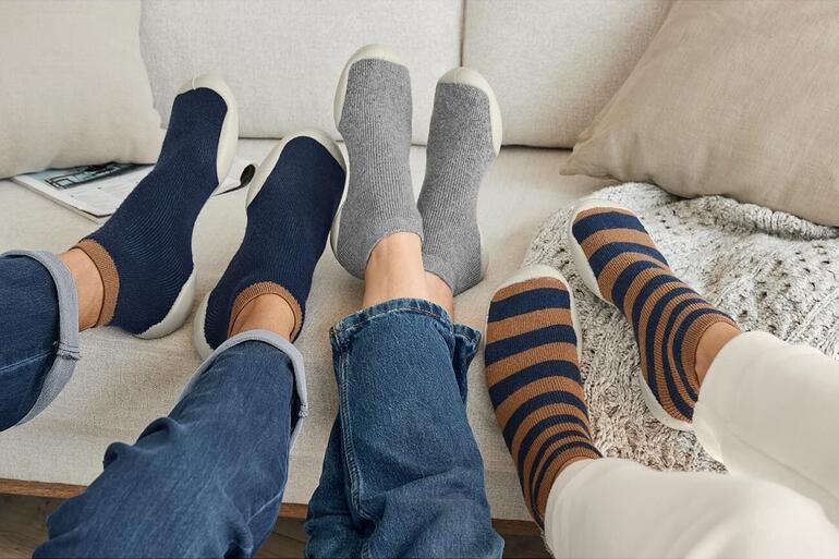 Trois paires de chaussettes de maison dans différentes couleurs sur un canapé.