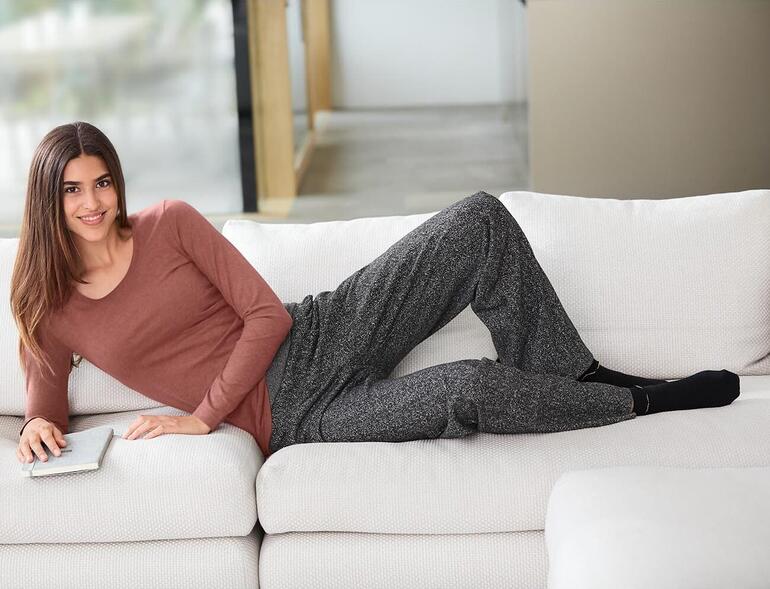 Marsala Femme portant un t-shirt Alpaga-Pima marron et un pantalon gris, détendue sur un canapé.