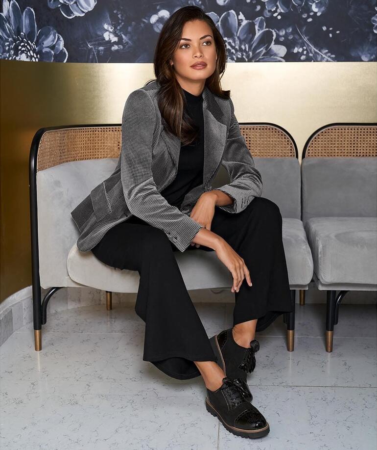 Femme dans un blazer en velours pied-de-poule, assise sur un banc.