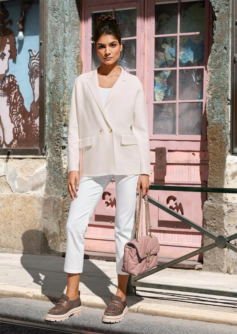 Crème Femme en blazer clair, pantalon marron, assise sur un banc.