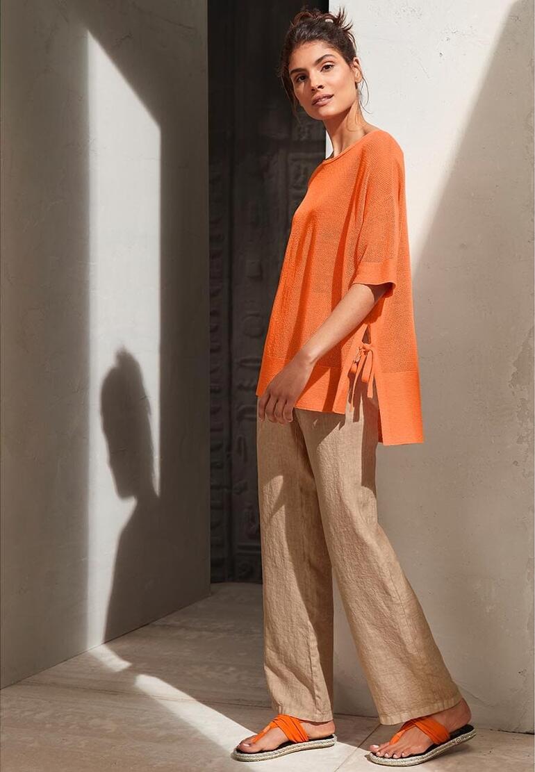 Orange Femme en haut orange et tongs, posée dans un espace minimaliste