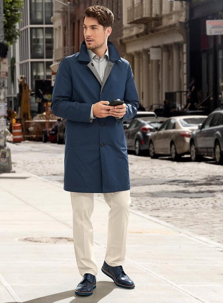 Homme en manteau réversible bleu dans la rue avec un smartphone