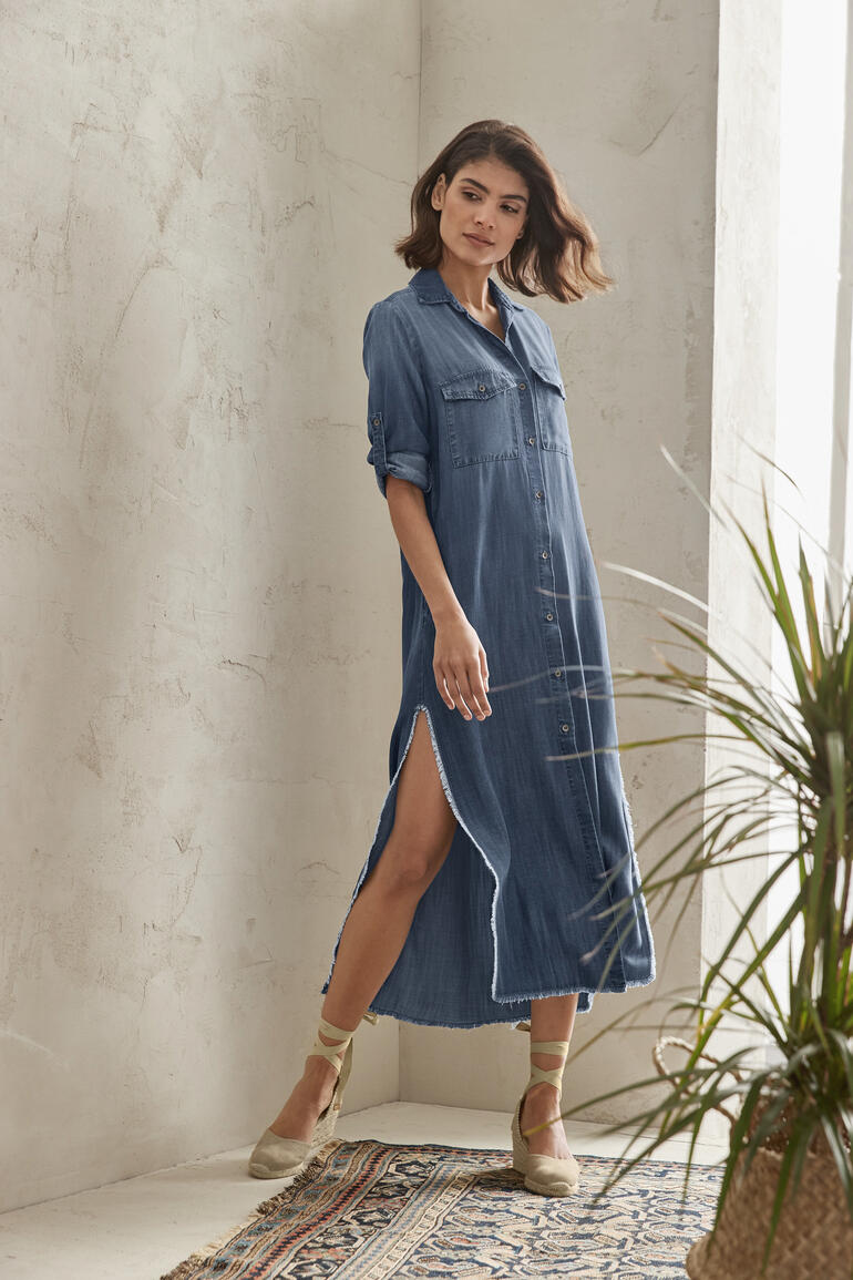 Femme en robe en jean avec une fente se tient dans une pose.