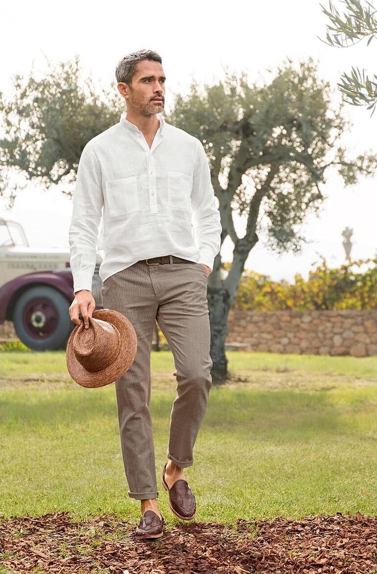 Chino estival à motif pied-de-poule Homme en chemise en lin légère avec un chapeau de paille dans un environnement méditerranéen.