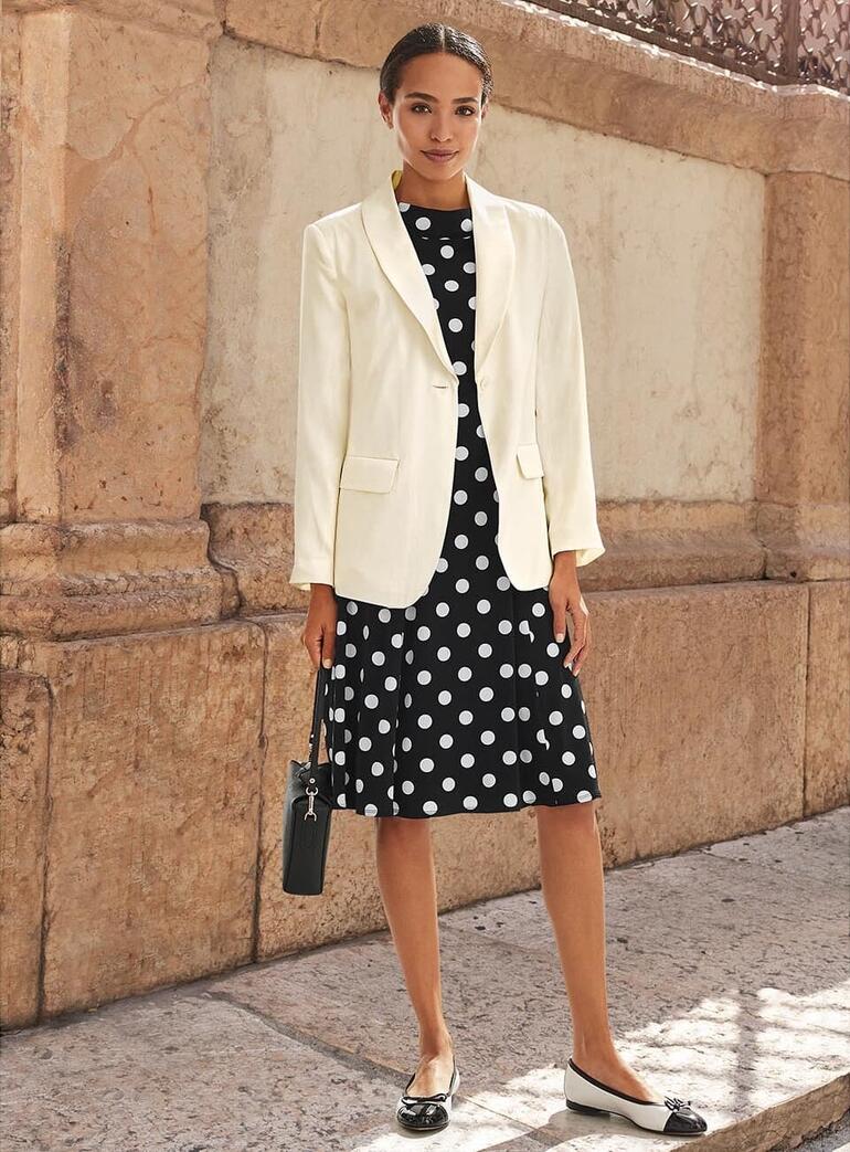 Blazer en soie blanche sur une robe à pois noire.