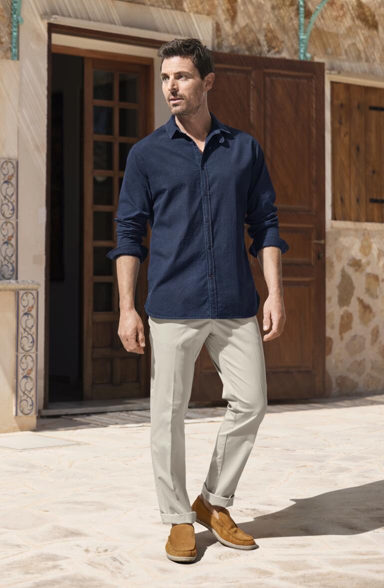 Homme portant une chemise en jean seersucker Oliver Spencer bleue et un pantalon clair, se tenant à l'extérieur.