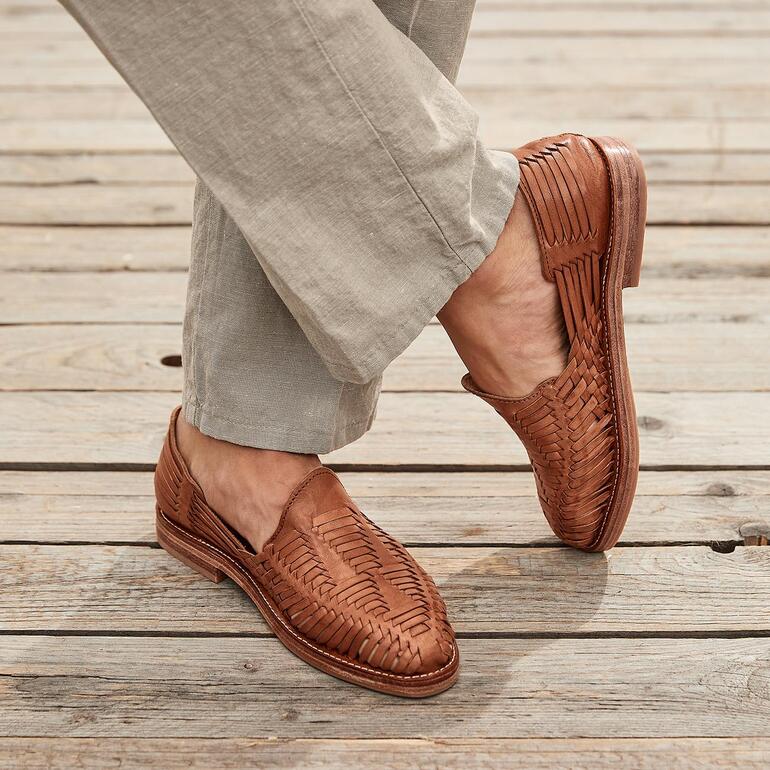 Huarache slip-on tressé de Cano en marron, porté avec un pantalon clair sur un sol en bois.