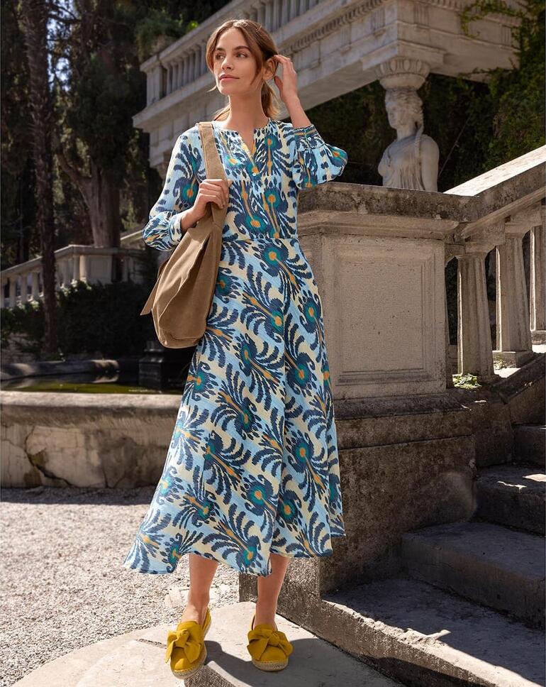 Robe Ikat Nimo With Love Femme portant une robe Ikat avec un motif coloré, se tenant sur un escalier à l'extérieur.