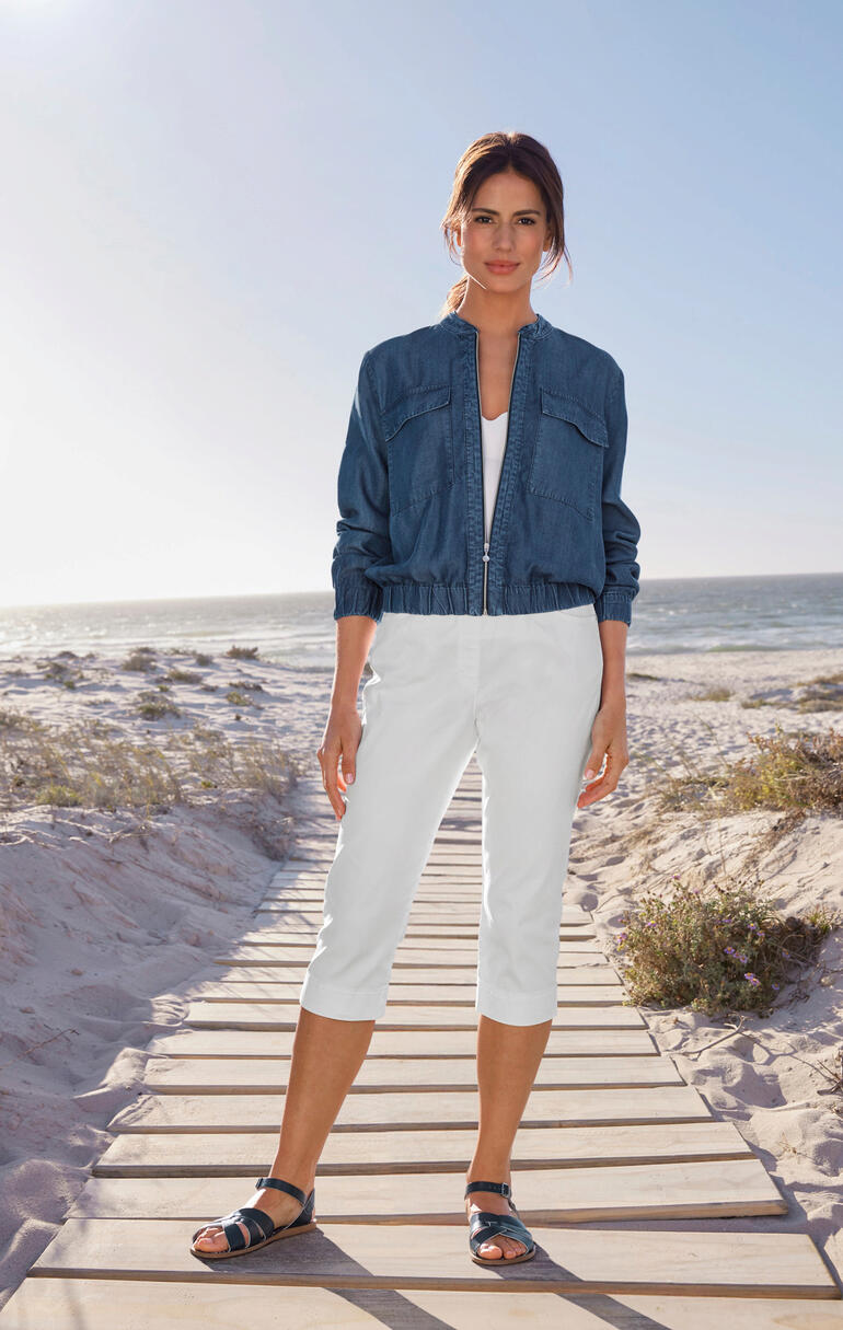 Femme portant un blouson en denim léger et un pantalon capri blanc se tient sur la plage.