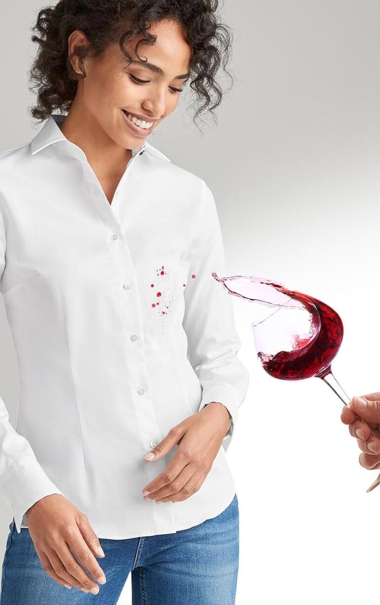 Femme souriante en blouse QuickClean blanche, éclaboussée de vin rouge.