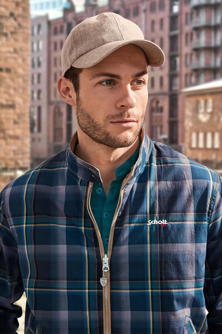 Homme avec une casquette et une chemise à carreaux, dehors dans un environnement urbain.
