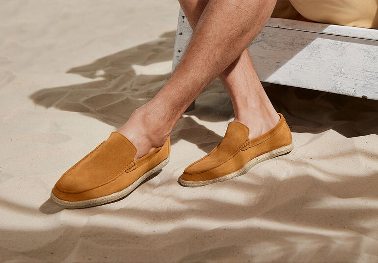 Chaussures pour hommes, mocassins espadrilles en brun, portés sur un sol de sable.