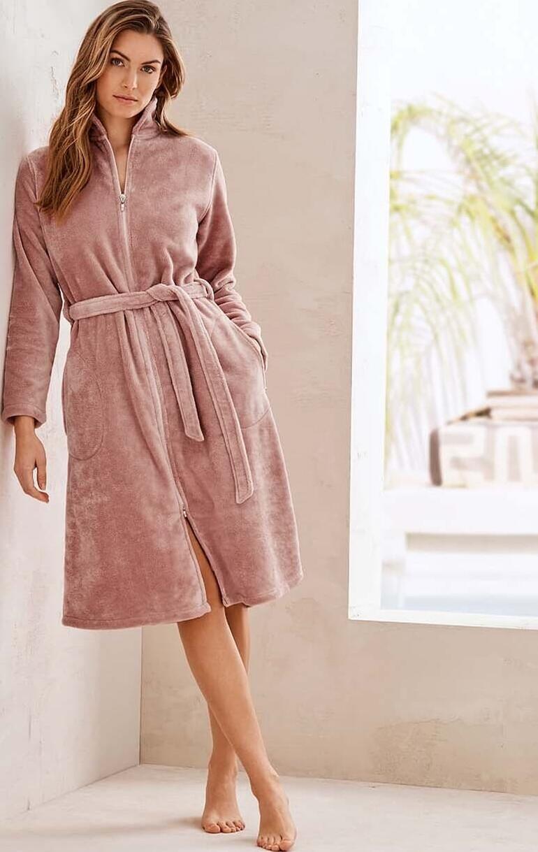 Femme en robe de bain Couture rose, debout contre un mur.