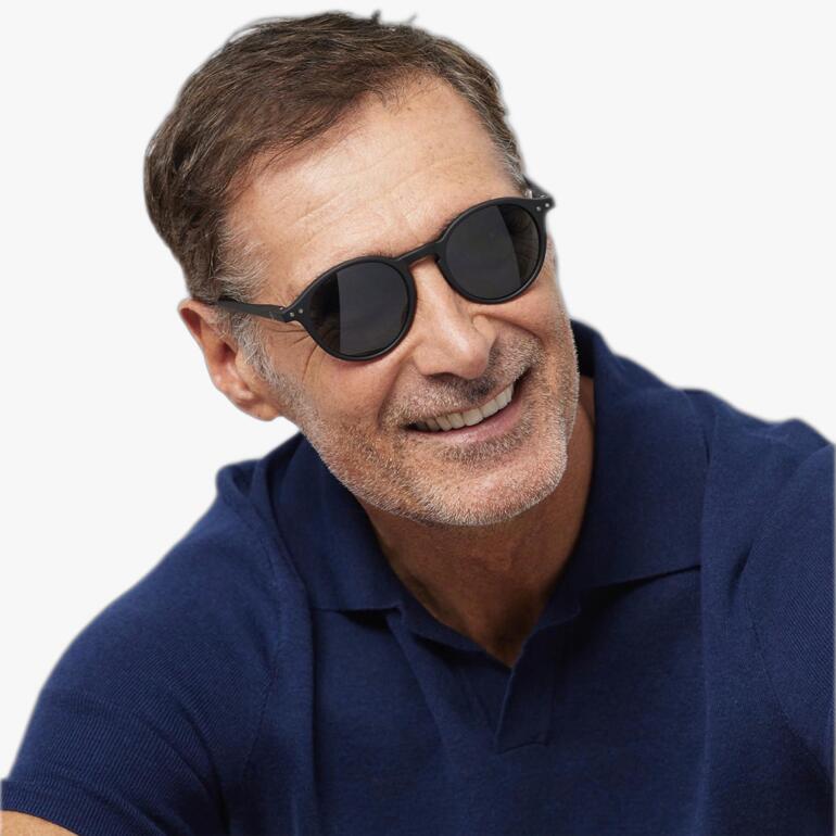 Homme souriant avec des lunettes de soleil, portant un polo bleu foncé.