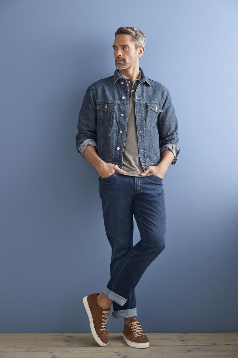 Bleu Homme en veste en jean en chanvre OCONI devant un fond bleu, avec un jeans et des baskets.