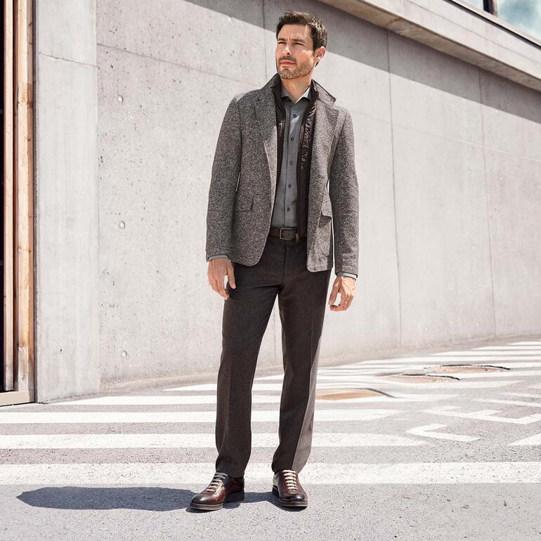 Homme en pantalon en cachemire et veste grises, posant sur une rue en béton.