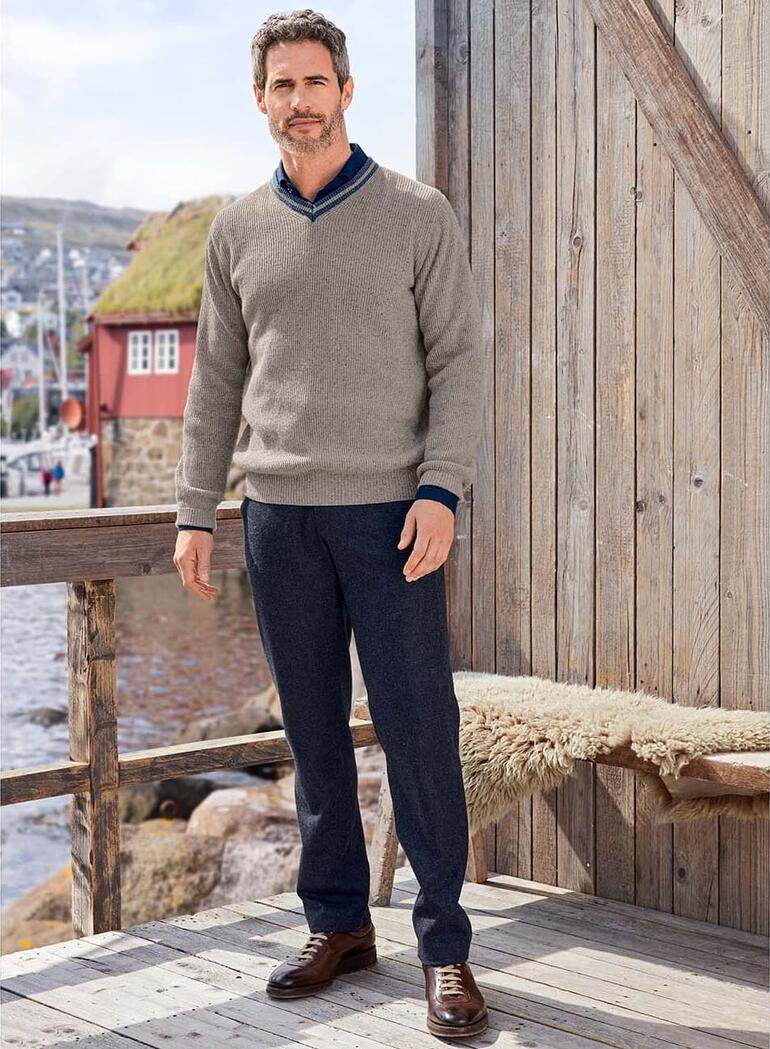 Pullover noble en tweed Junghans 1954 Homme en pull en tweed gris devant une façade en bois.