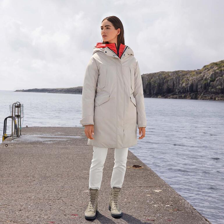 Pantalon ecorepel® Kris Reutter Femme en manteau gris se tenant sur une promenade portuaire.