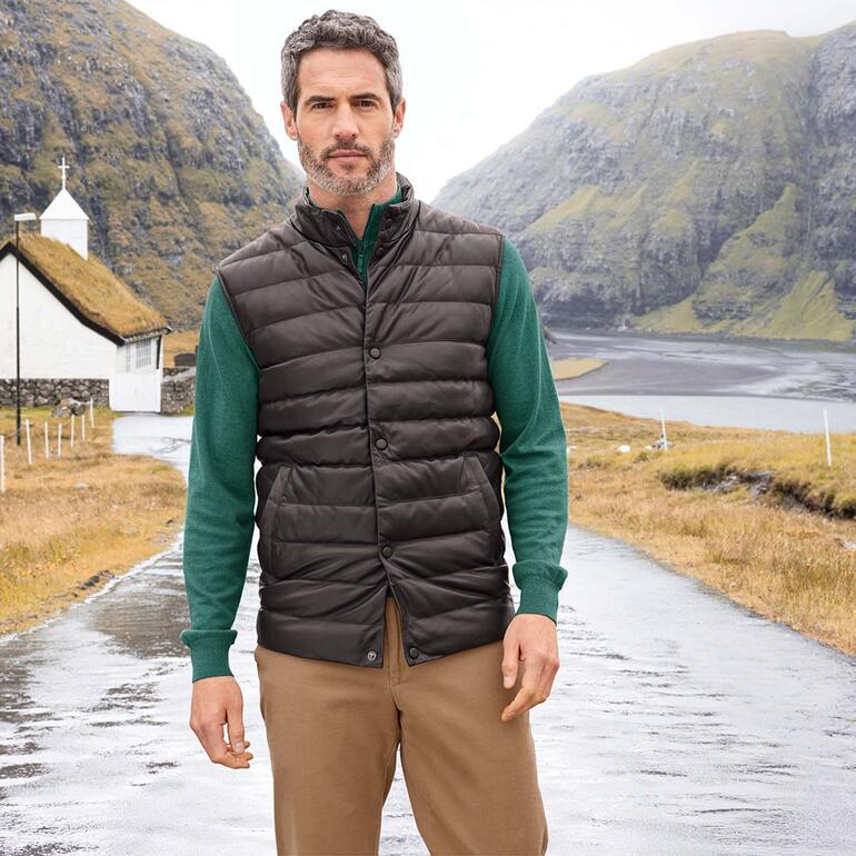 Homme en gilet matelassé en cuir d'agneau noir et en pull toute saison vert à l'extérieur.