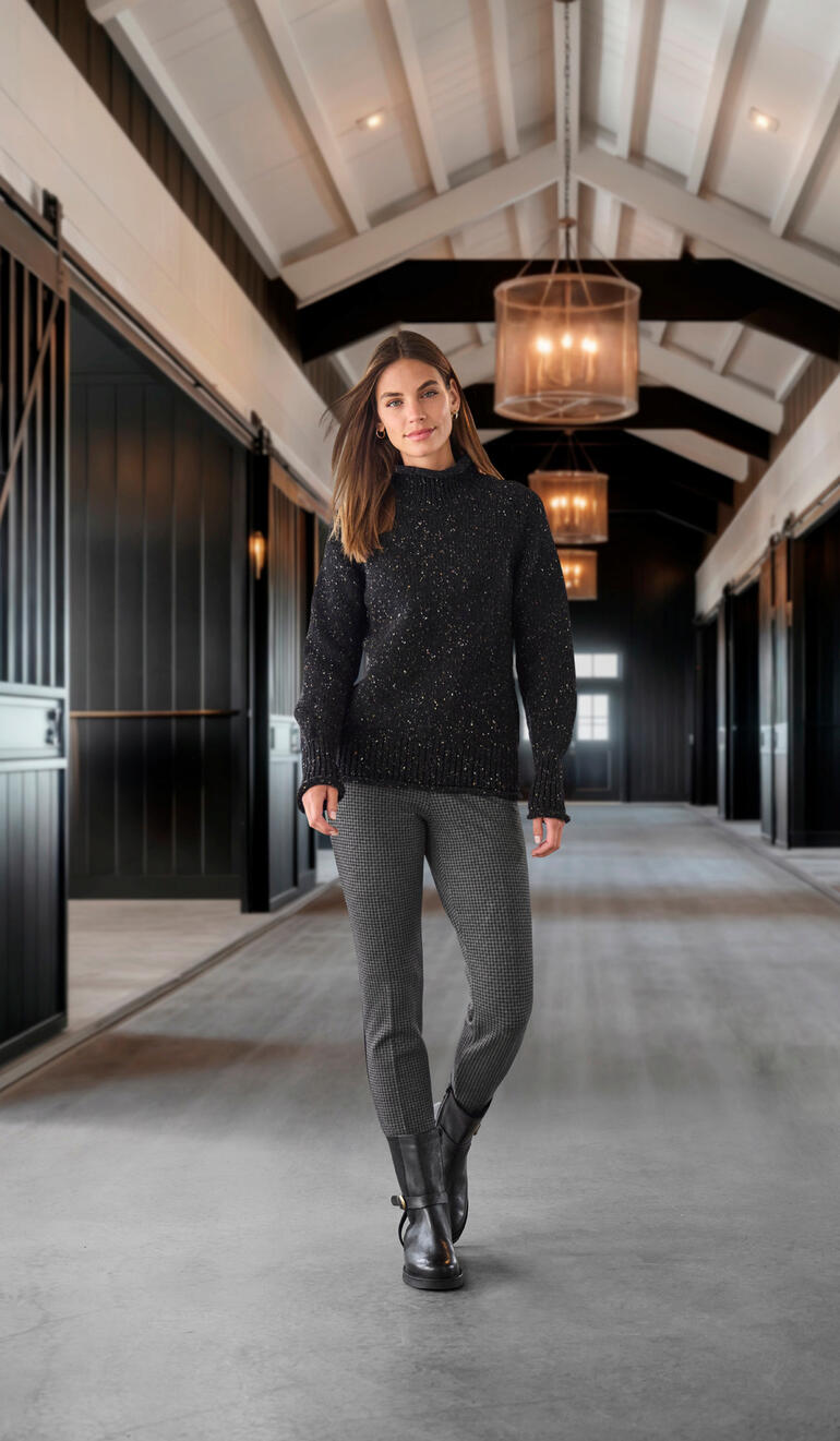 Bottines de motard élégantes Werner Femme en pull noir et pantalon pied-de-poule dans un hall moderne.