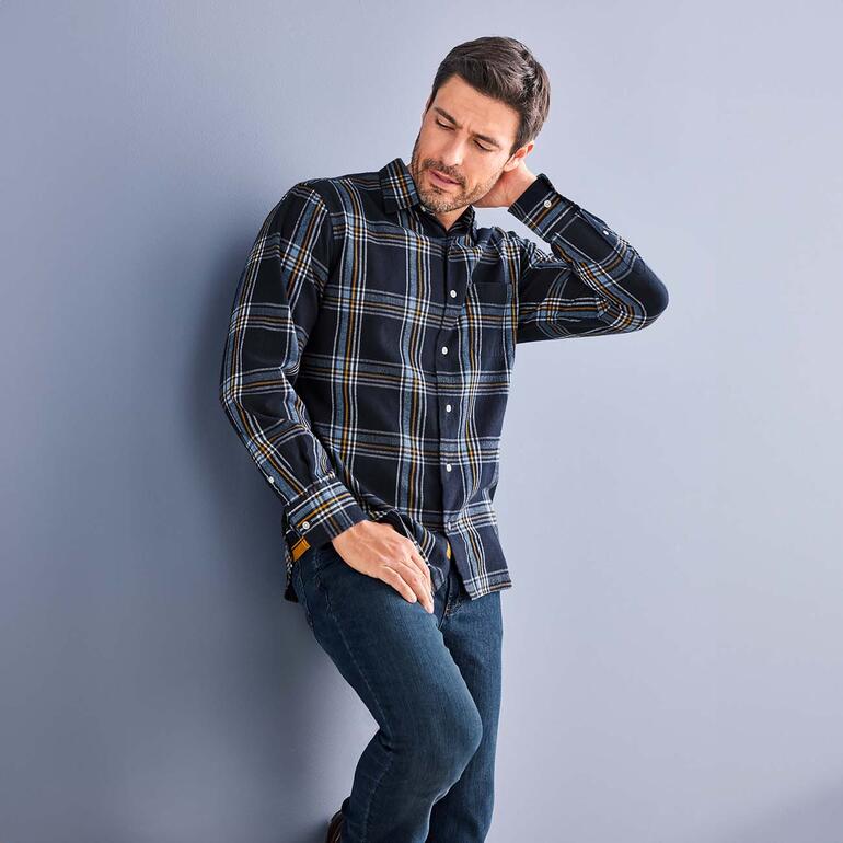 Chemise hivernale Madras OMTC Homme en chemise à carreaux OMTC Winter Madras appuyé contre un mur.