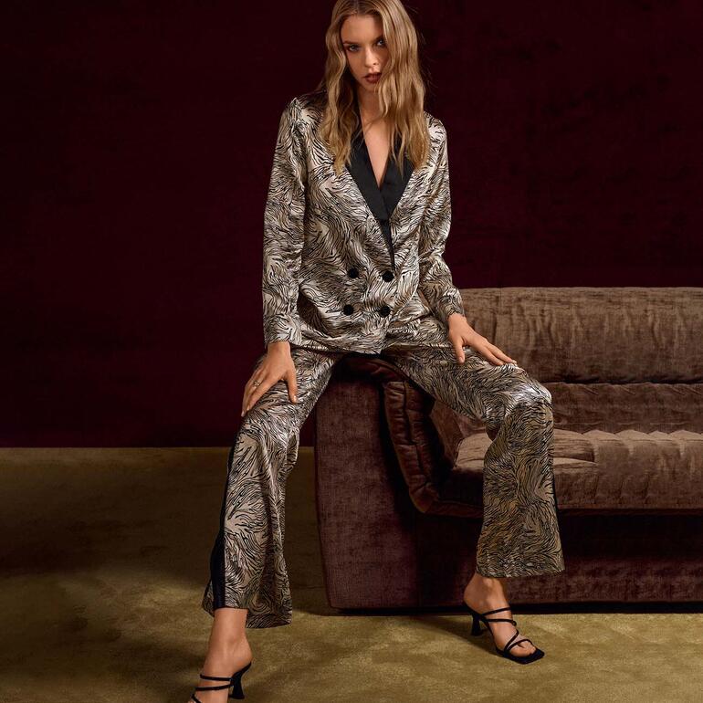 Femme en pyjama à motifs, avec veste et pantalon, assise sur un canapé.