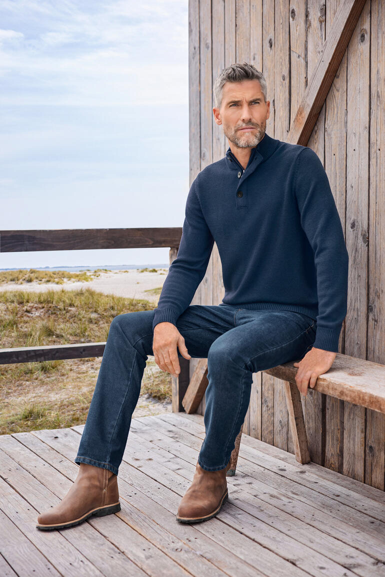 Troyer outdoor Alan Paine Homme assis dans un pull d'extérieur bleu marine sur une terrasse.