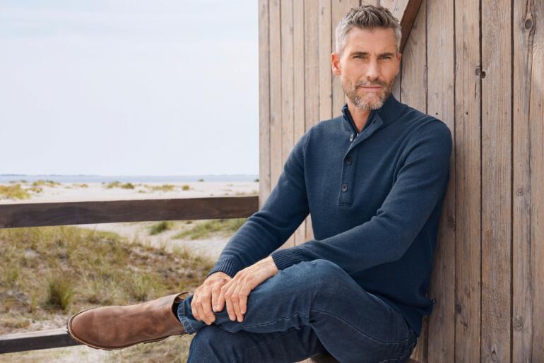 Homme en pull bleu marine à col court sur une terrasse.