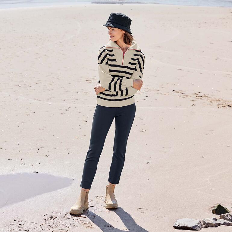 Troyer en laine mérinos Saint James Femme portant un pull en merino rayé et un chapeau à la plage.
