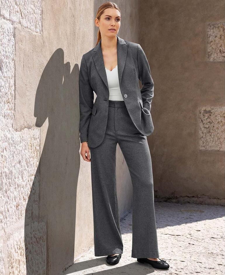 Blazer et Pantalon Femme debout en blazer gris avec pantalon contre un mur