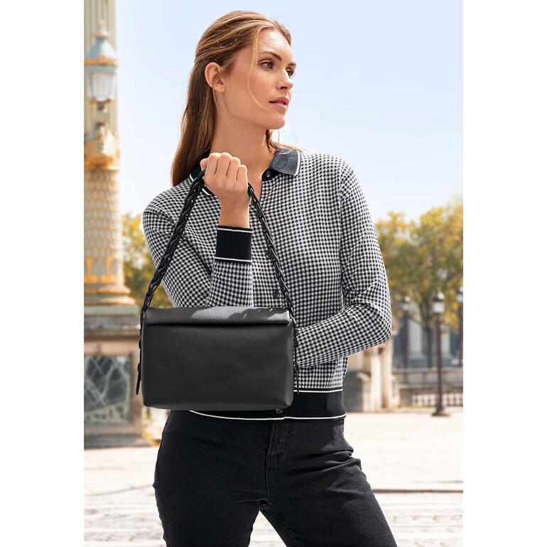 Femme avec un sac noir posant devant un paysage urbain.