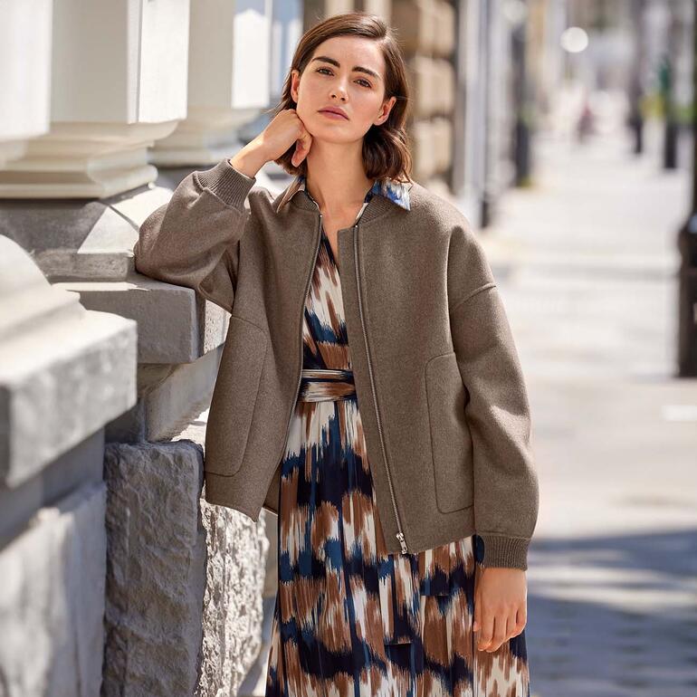 Femme en robe flatteuse et veste décontractée se tenant à un coin de rue.