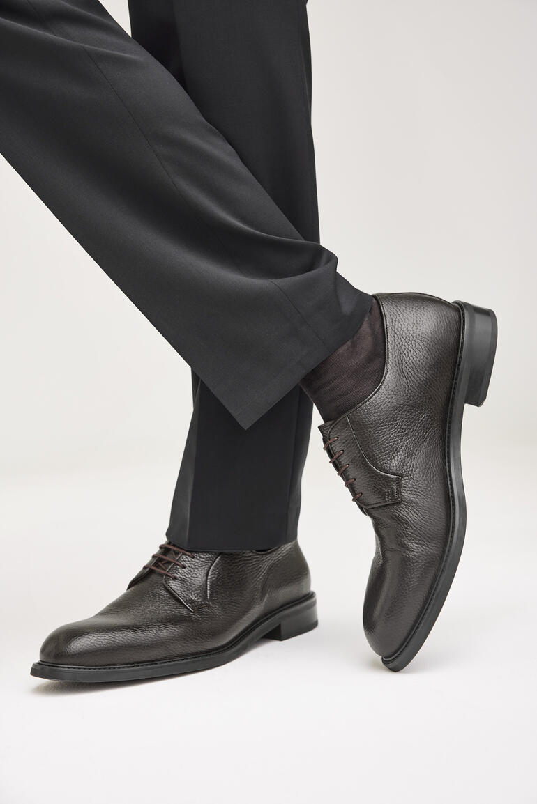 Homme portant des chaussures de bureau en cuir de cerf marron, assis à moitié dans un costume.