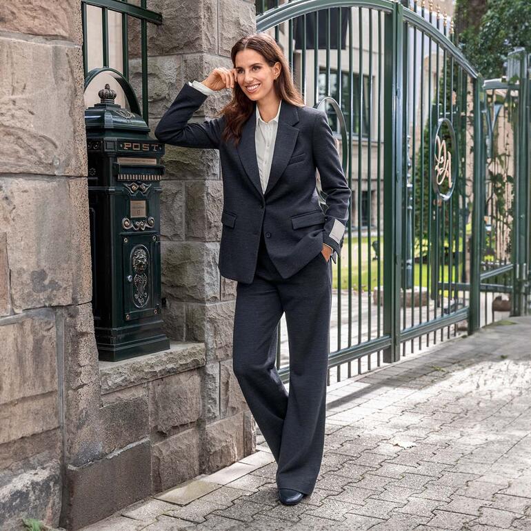 Femme en blazer et pantalon en jersey de laine noir devant un bâtiment historique.