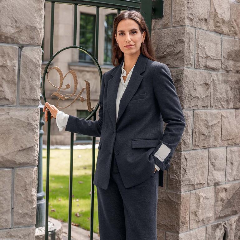 Portrait d'une femme en blazer noir appuyée contre une colonne.