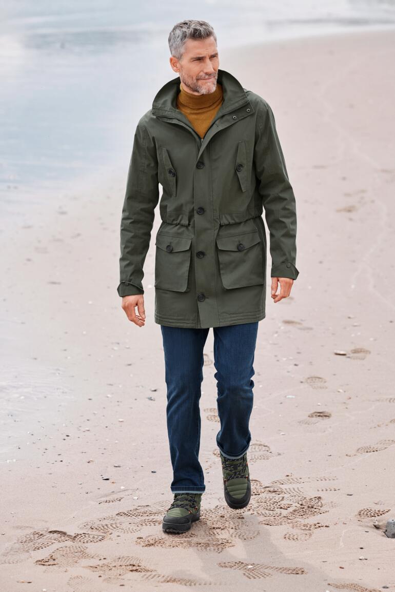 Homme en parka en coton vert avec poches marchant sur la plage.