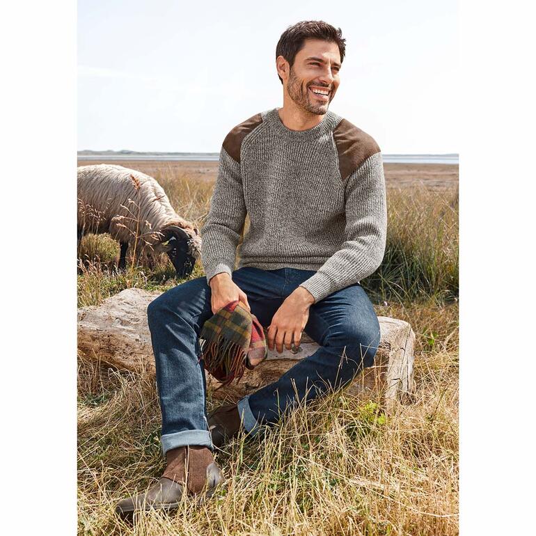Jean cachemire confortable Homme assis sur une souche dans la nature, portant un pull gris.