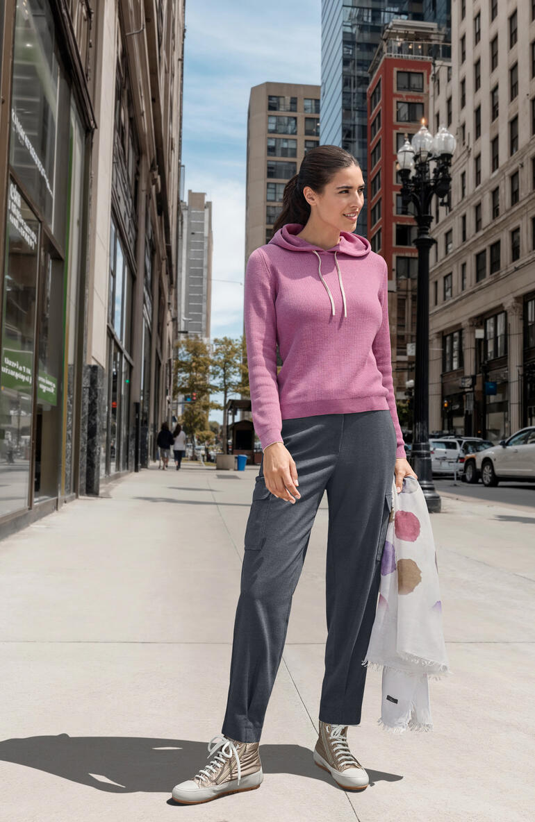 Sneaker glamour Candice Cooper Femme en hoodie rose se tient sur une rue de la ville.