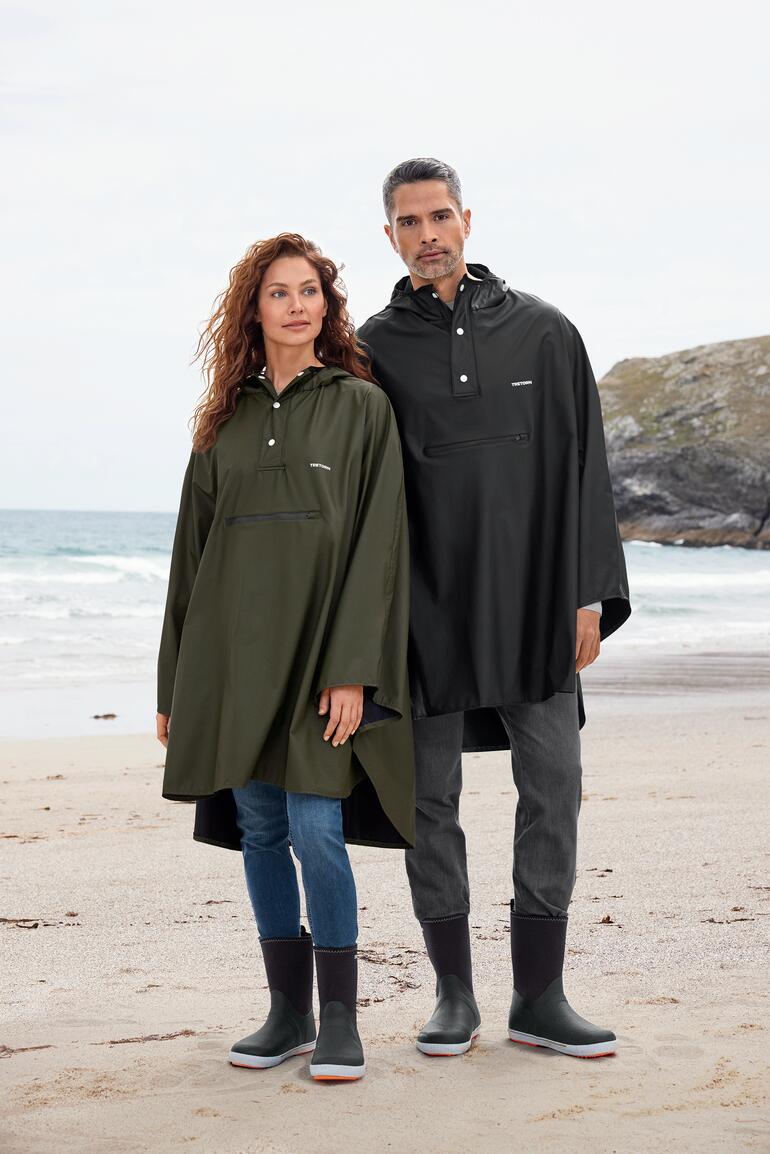 Olive et Noir Cape de pluie unisexe Tretorn, portée par un homme et une femme sur la plage.