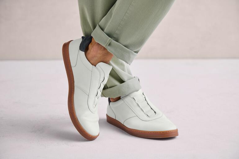 Blanc Homme portant des chaussures OCONI slip-on blanches sur un fond gris.