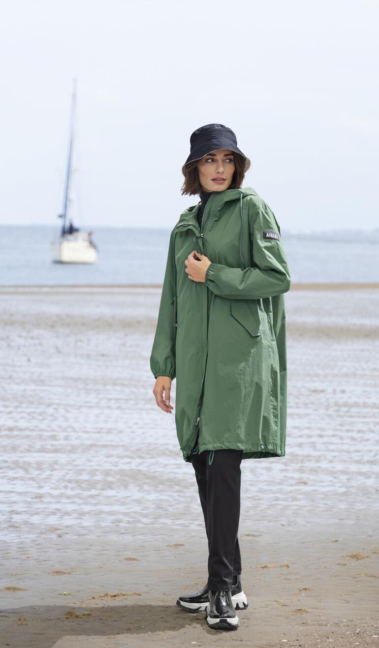 Femme en imperméable vert et chaussures de type Chelsea sur la plage.