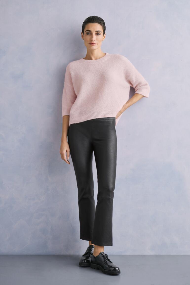 Rosé Femme en pull rose et pantalon en cuir kick-flare noir sur fond gris.