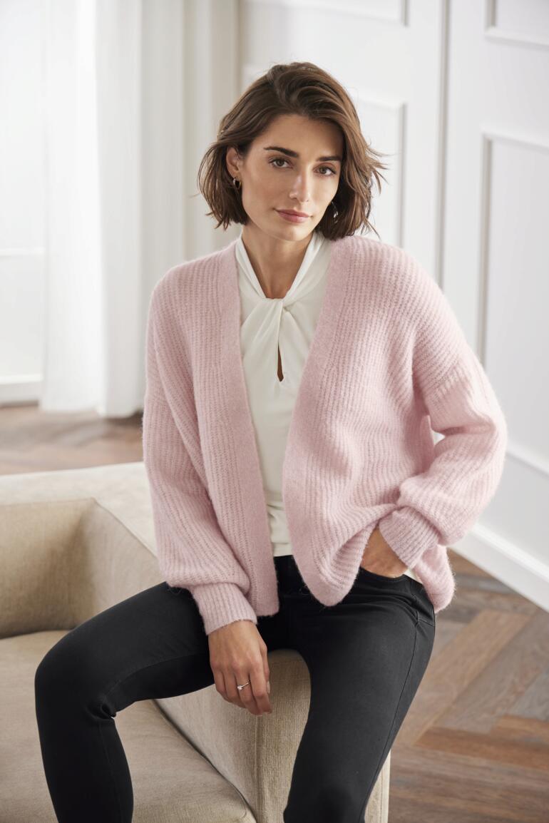 Femme assise dans un cardigan moelleux Junghans 1954 en rose.
